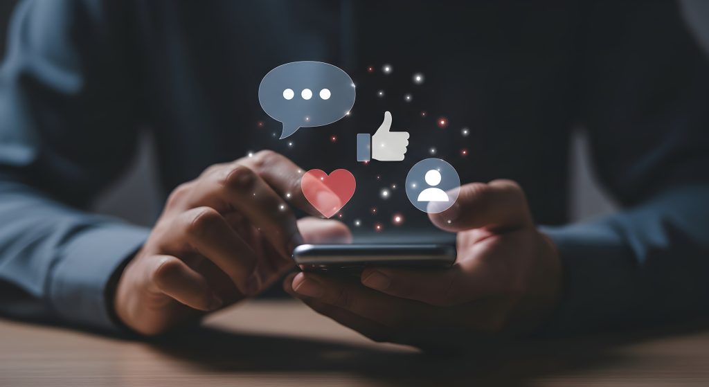 AdobeStock 1698275709 Personne utilisant un téléphone d'où émanent des icônes de réseaux sociaux : like, commentaire