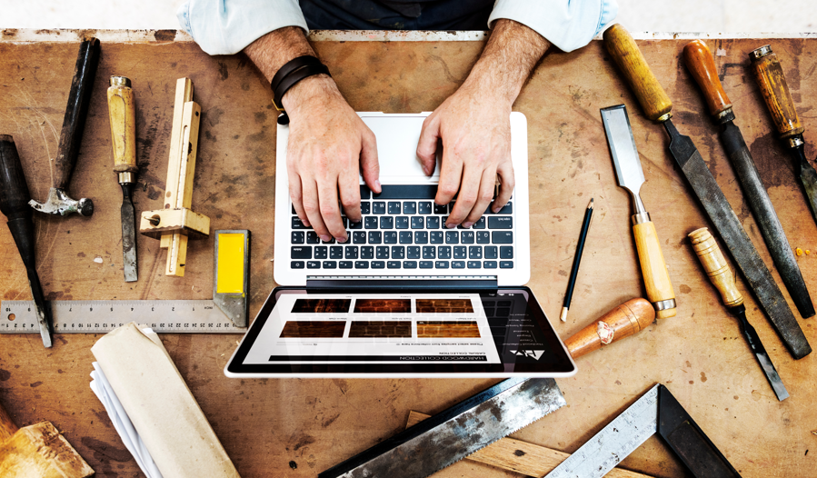 Un artisan travaillant sur un ordinateur portable posé sur un établi encombré d'outils dans un atelier