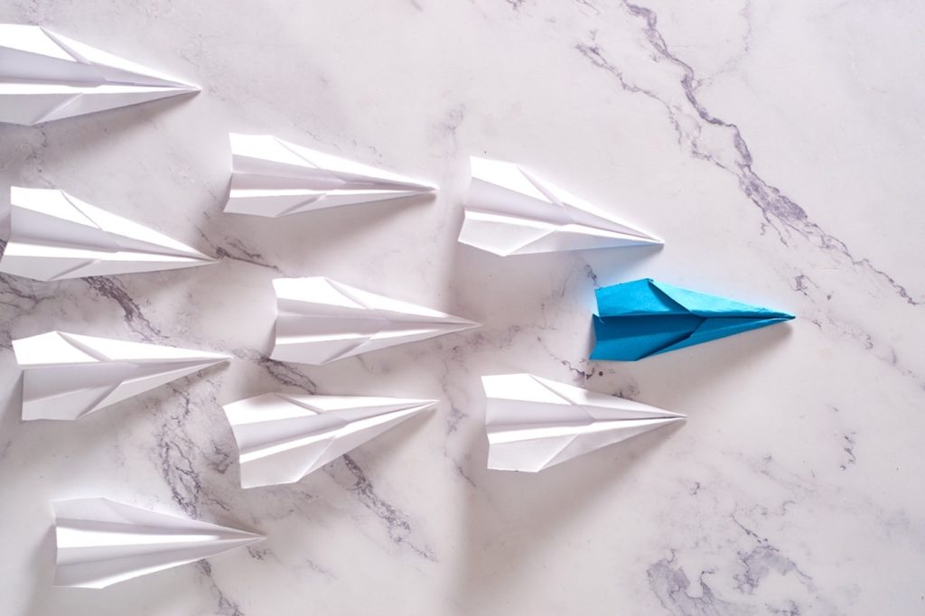 Image1 Avion en papier bleu volant avec des avions blancs, illustrant la différenciation marketing